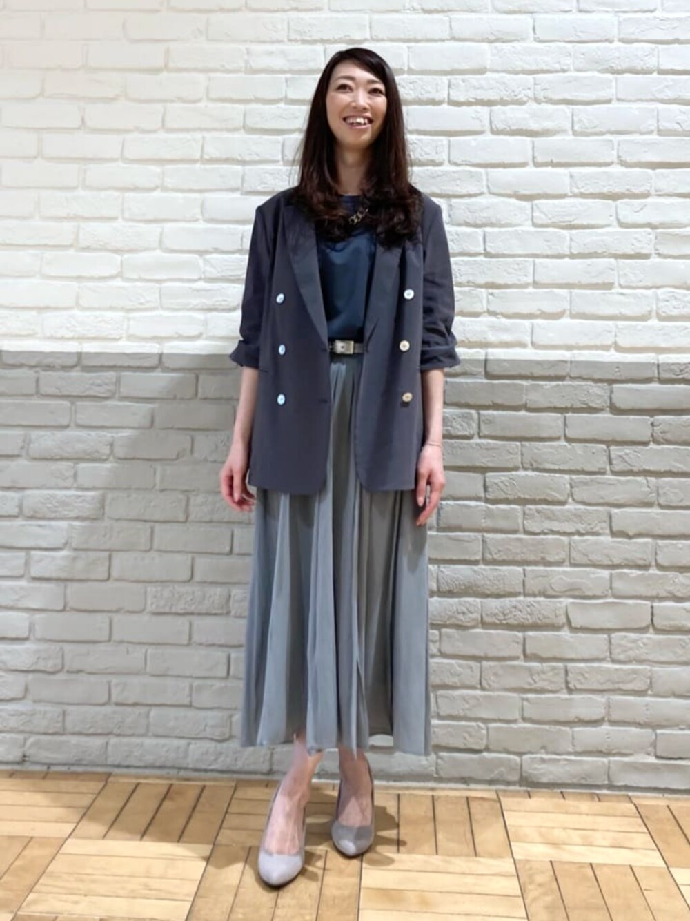 グレー系のテーラードジャケット、グリーン系のスカート、ブラック系のタンクトップを着用したレディースの春コーディネートの1枚目の写真