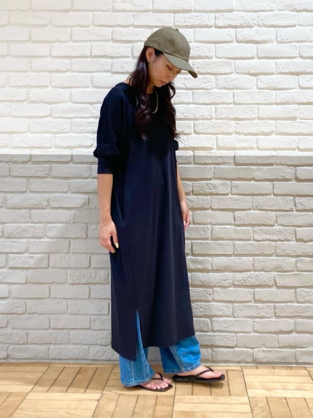 ブラック系のワンピース、ブルー系のデニムパンツ、グリーン系のキャップを着用したレディースの秋コーディネートの1枚目の写真