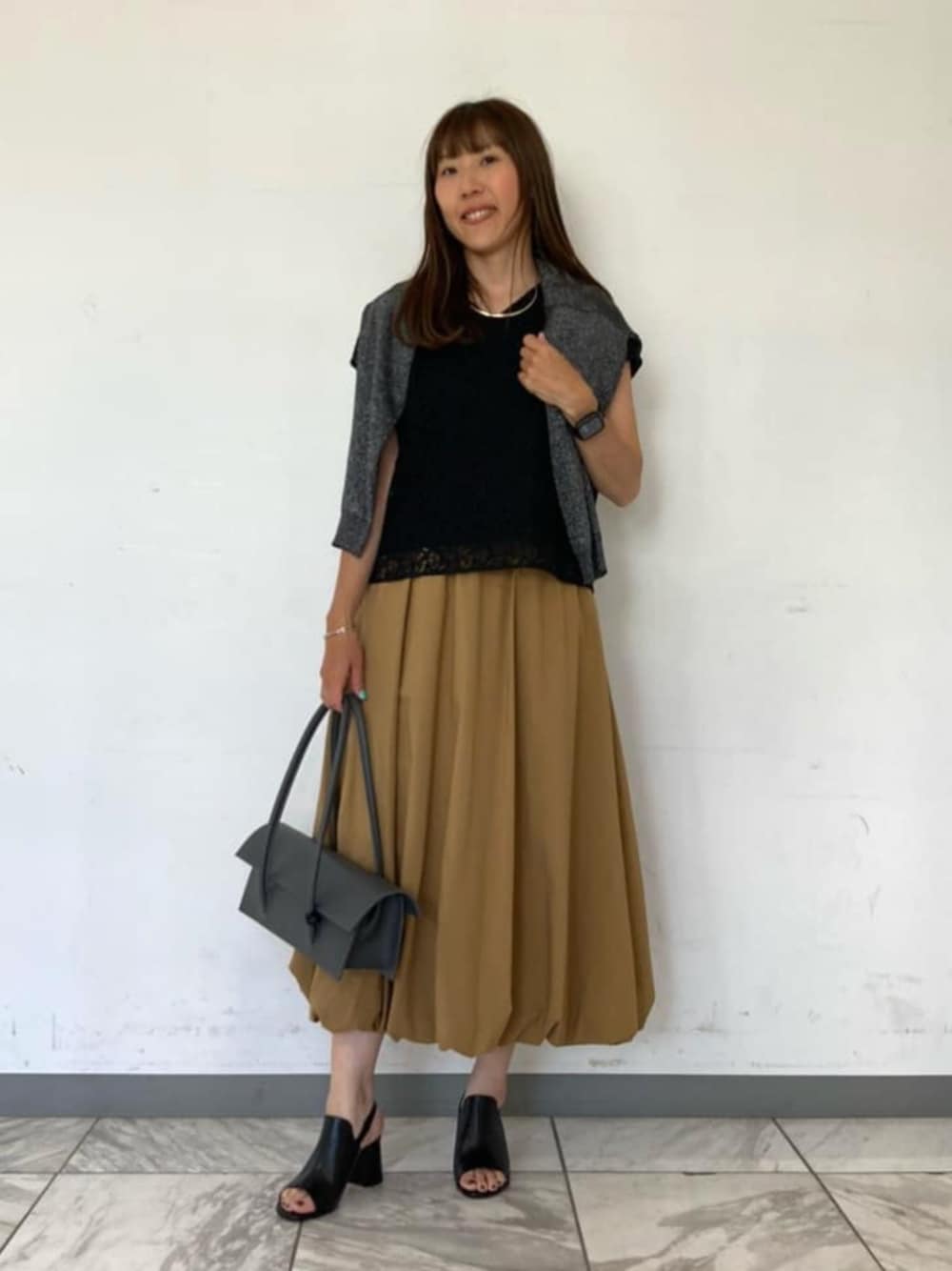 ブラック系のシャツ/ブラウス、ブラック系のサンダル、グレー系のスカートを着用したレディースの春コーディネートの1枚目の写真