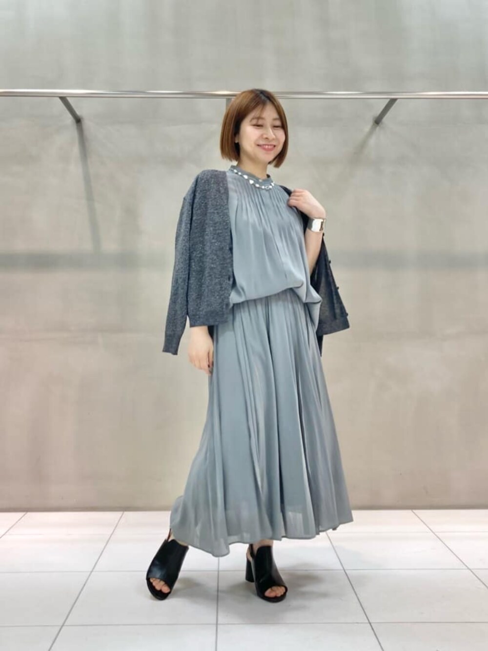 ブラック系のサンダル、グレー系のカーディガン/ボレロ、グリーン系のスカートを着用したレディースの春コーディネートの1枚目の写真