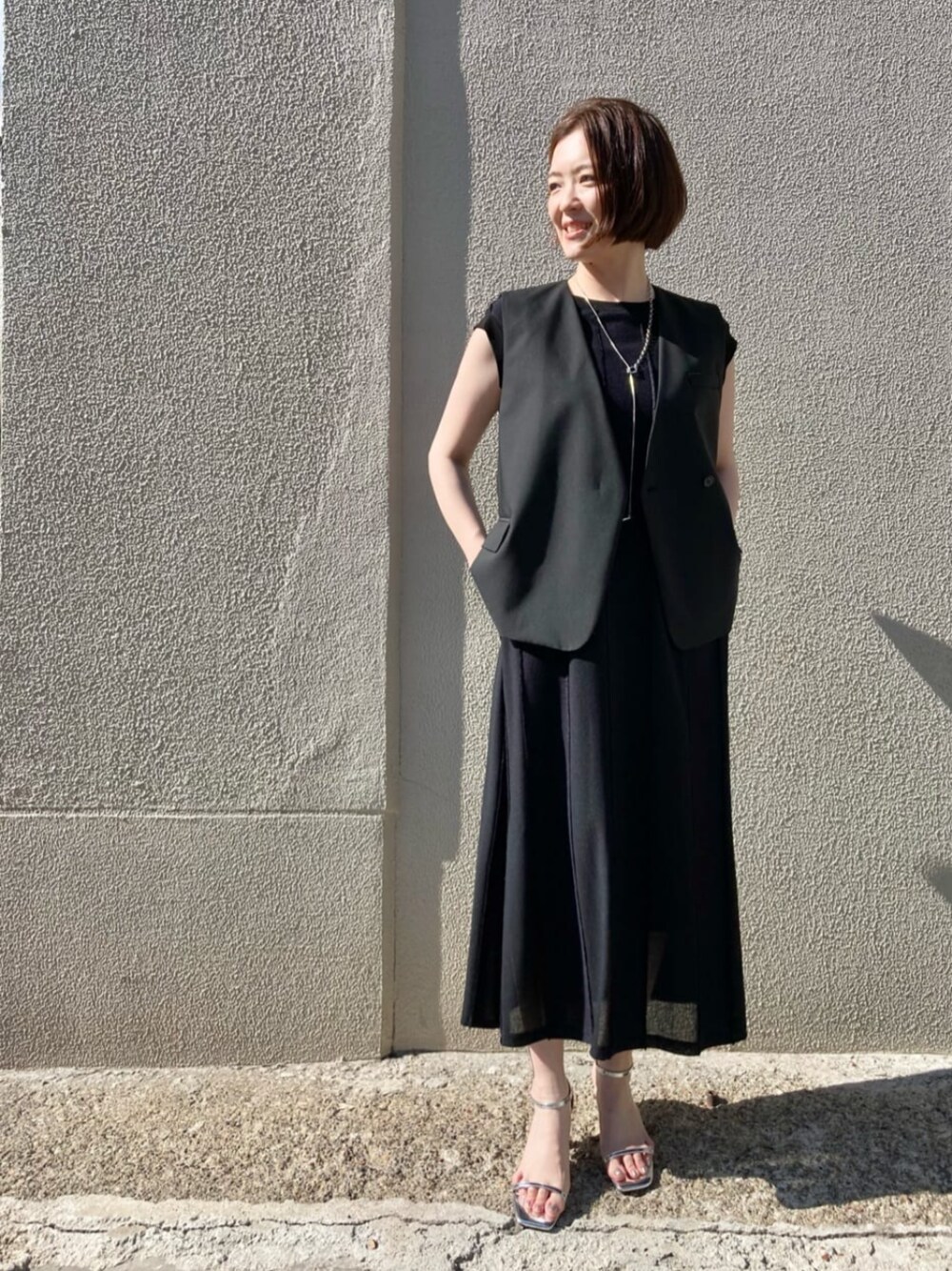 ブラック系のベストを着用したレディースの夏コーディネートの1枚目の写真