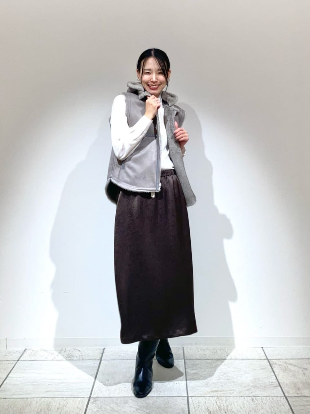 ベージュ系のベスト、ブラック系のスカート、ホワイト系のシャツ/ブラウスを着用したレディースの冬コーディネートの1枚目の写真
