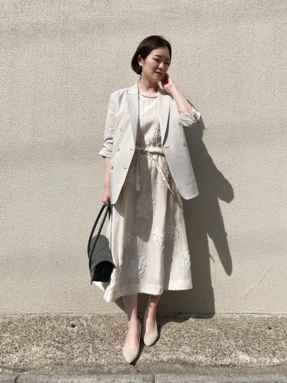 ベージュ系のテーラードジャケット、ベージュ系のワンピース、ゴールド系のネックレスを着用したレディースの夏コーディネートの1枚目の写真