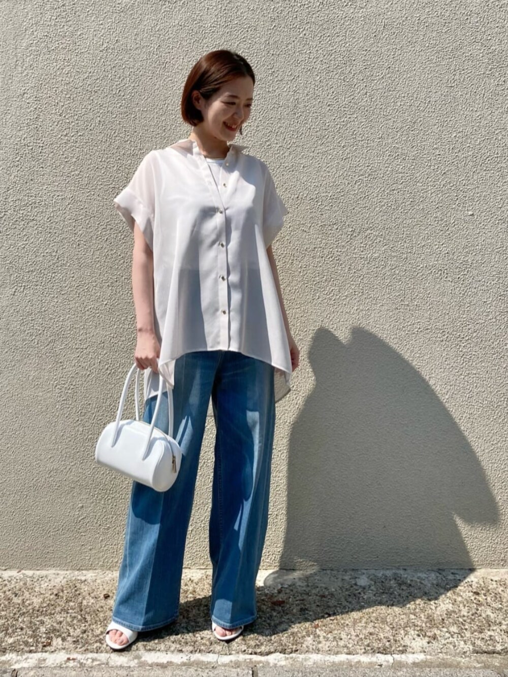 ブルー系のデニムパンツ、ホワイト系のサンダル、ホワイト系のシャツ/ブラウスを着用したレディースの夏コーディネートの1枚目の写真