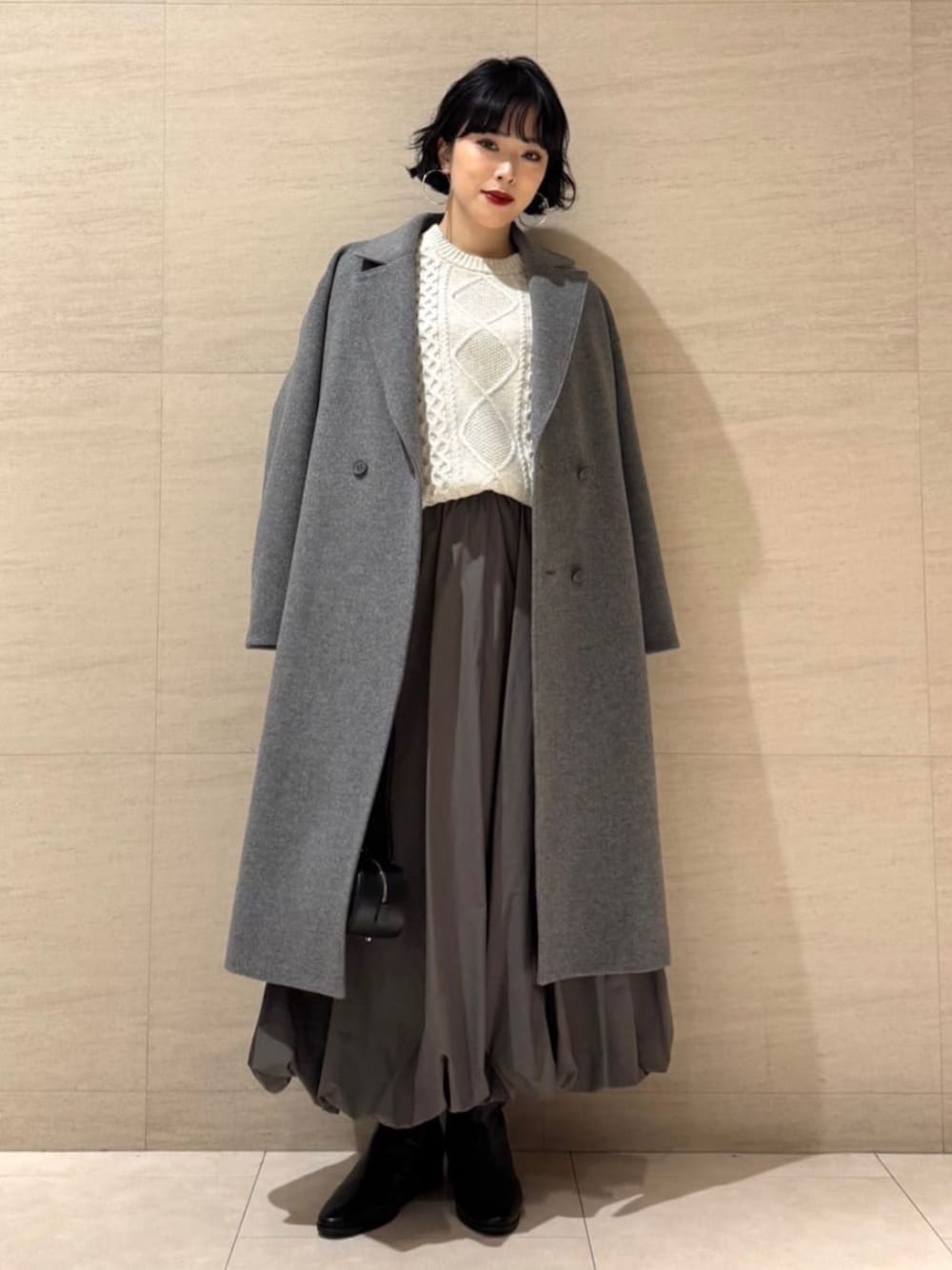 グレー系のチェスターコート、グリーン系のスカートを着用したレディースの冬コーディネートの1枚目の写真