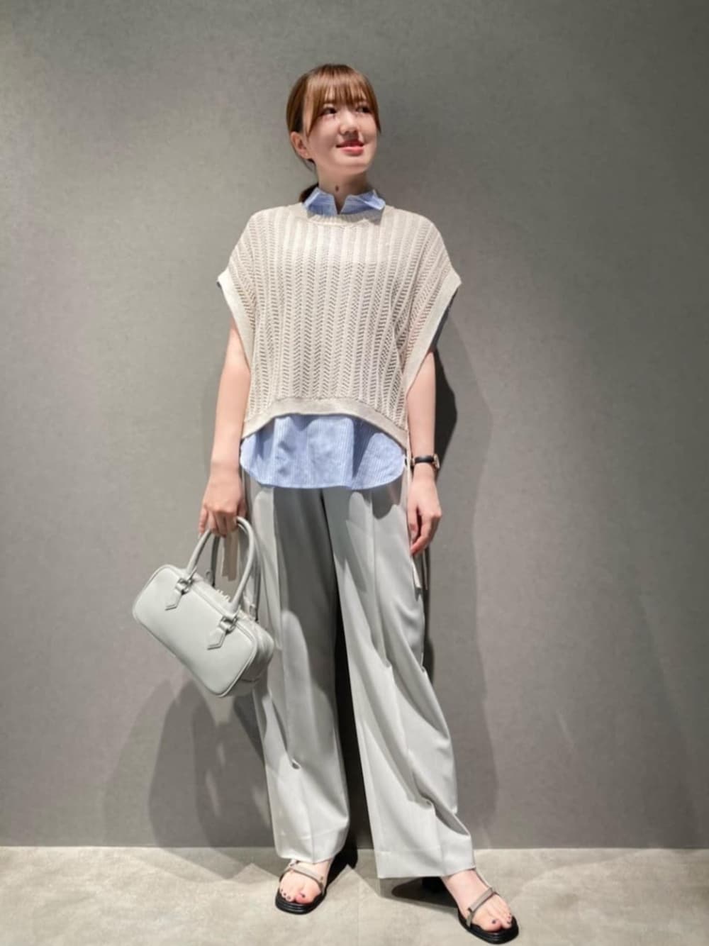 グレー系のボストンバッグ、グレー系のサンダル、ホワイト系のアンサンブルを着用したレディースの夏コーディネートの1枚目の写真