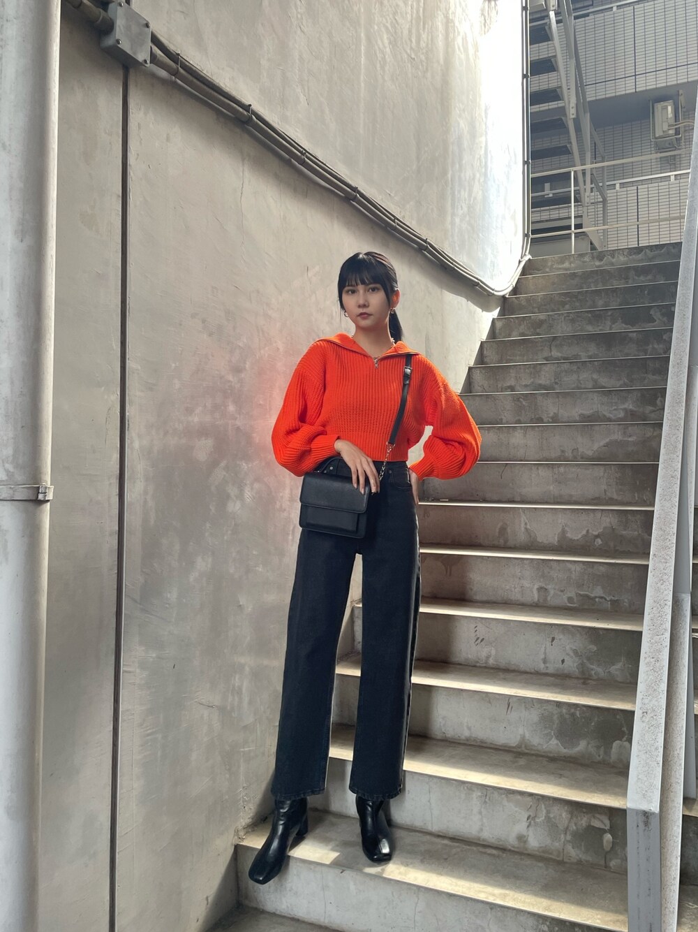 オレンジ系のニット/セーター、ブラック系のデニムパンツ、ブラック系のブーツを着用したレディースの夏コーディネートの1枚目の写真