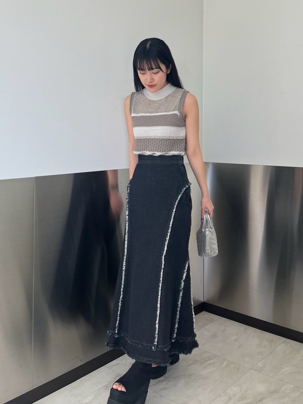 グレー系のニット/セーター、ブラック系のデニムスカート、ブラック系のブーツを着用したレディースの春コーディネートの1枚目の写真