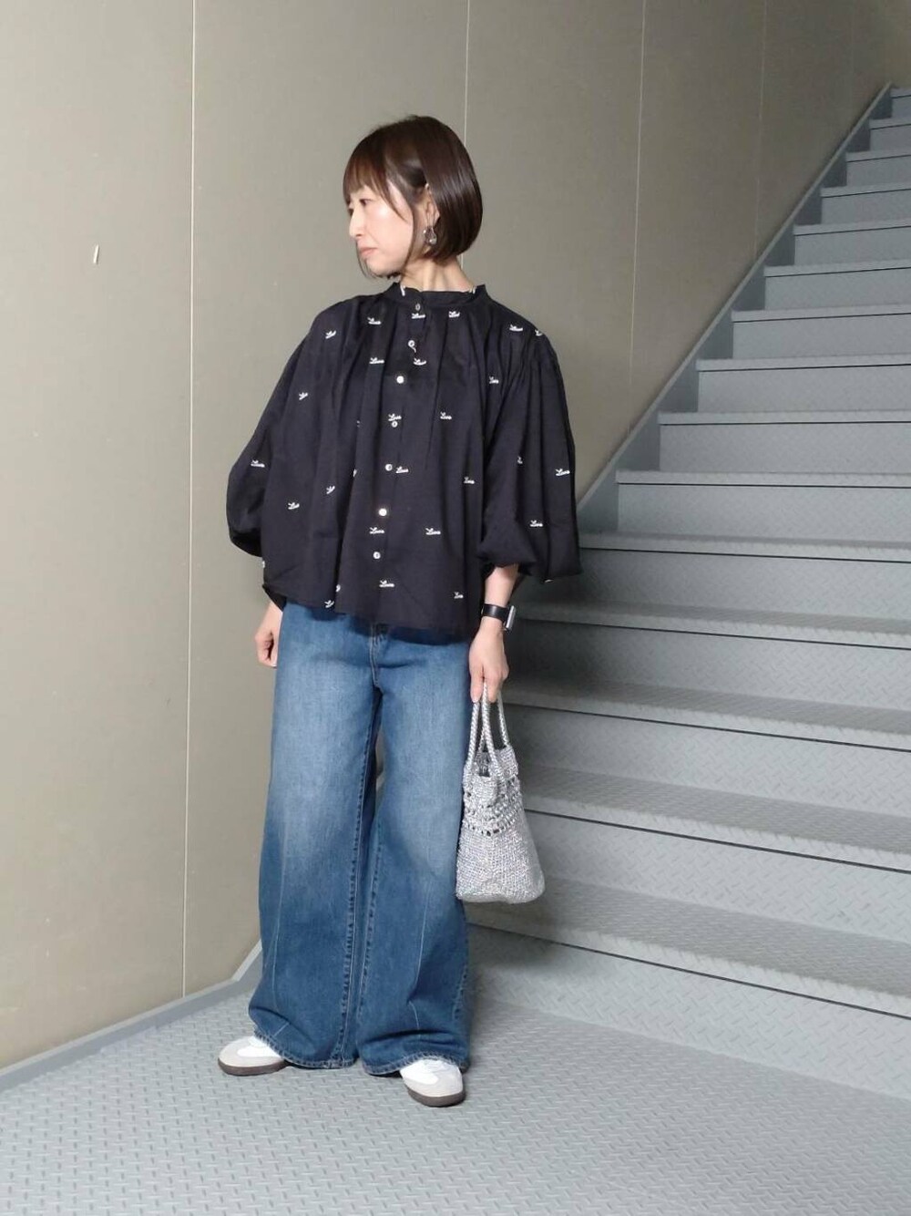 シルバー系のショルダーバッグ、ブルー系のデニムパンツ、ブラック系のシャツ/ブラウスを着用したレディースの春コーディネートの1枚目の写真