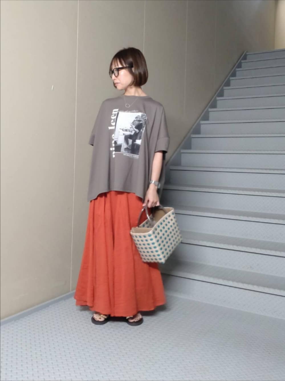グレー系のTシャツ/カットソー、レッド系のスカート、ブラウン系のサンダルを着用したレディースの夏コーディネートの1枚目の写真