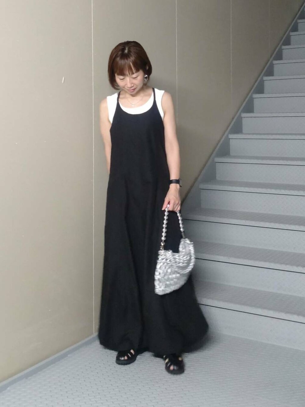 シルバー系のハンドバッグ、ホワイト系のタンクトップ、ブラック系のワンピースを着用したレディースの夏コーディネートの1枚目の写真