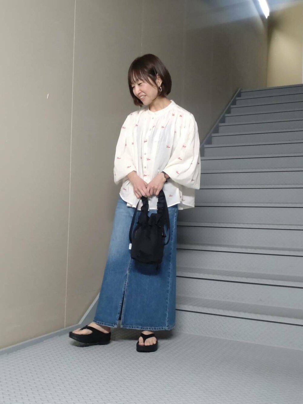 ブラック系のショルダーバッグ、ブラック系のサンダル、ブルー系のスカートを着用したレディースの春コーディネートの1枚目の写真