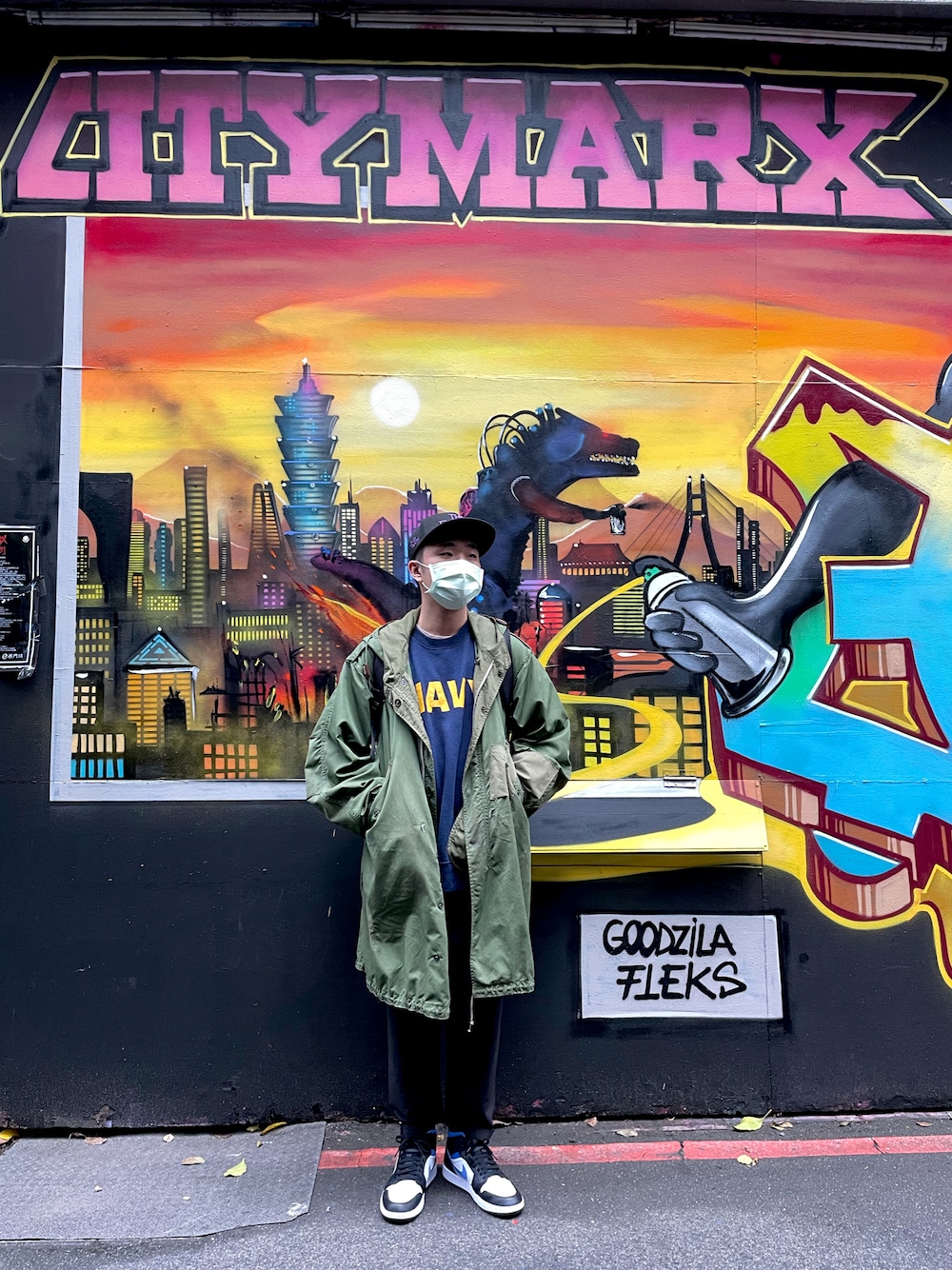 グリーン系のミリタリージャケット、ブラック系のチノパンツ、ブルー系のスニーカーを着用したメンズの秋コーディネートの1枚目の写真