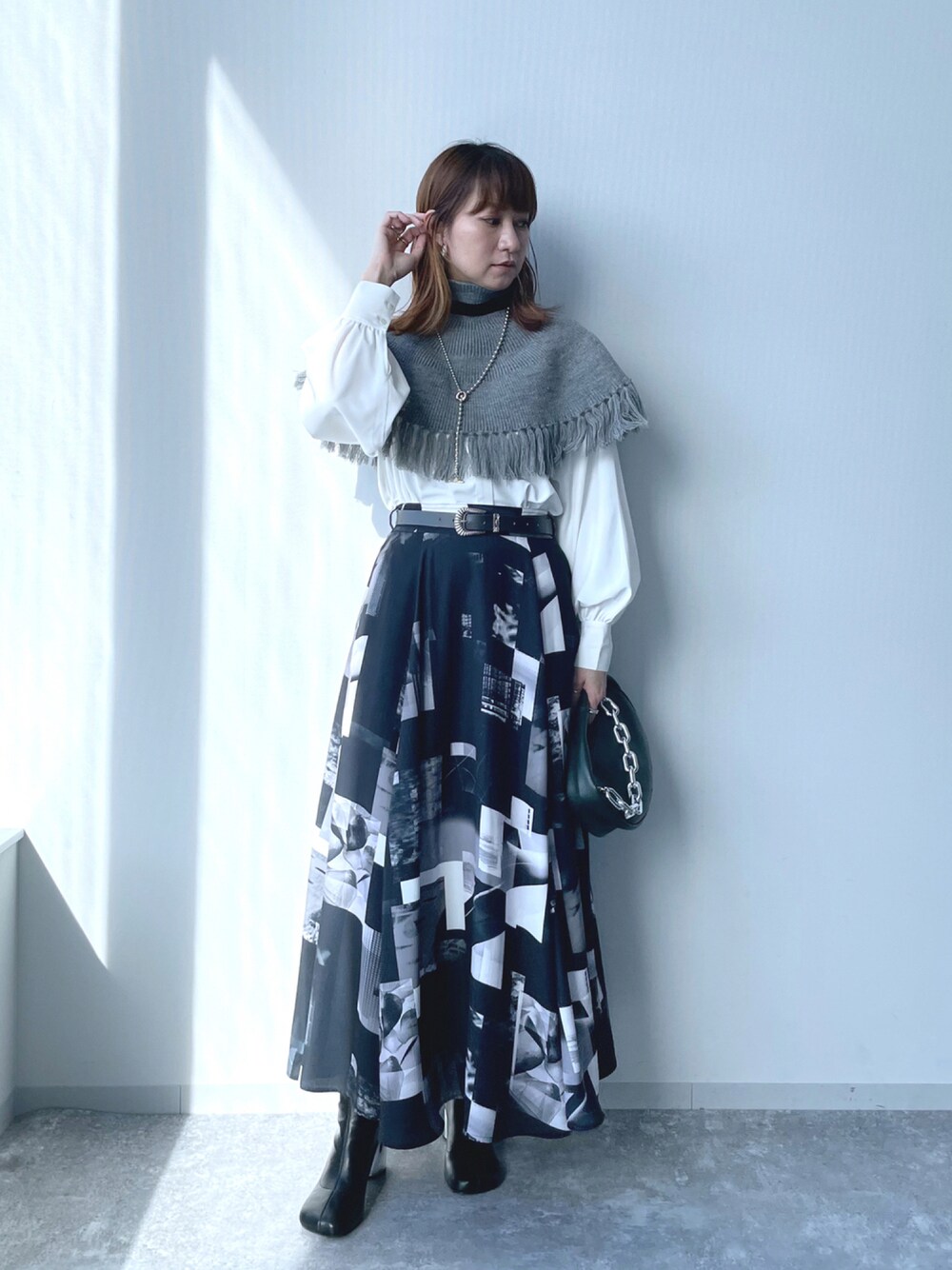 ブラック系のブーツ、ブラック系のスカート、グリーン系のハンドバッグを着用したレディースの秋コーディネートの1枚目の写真