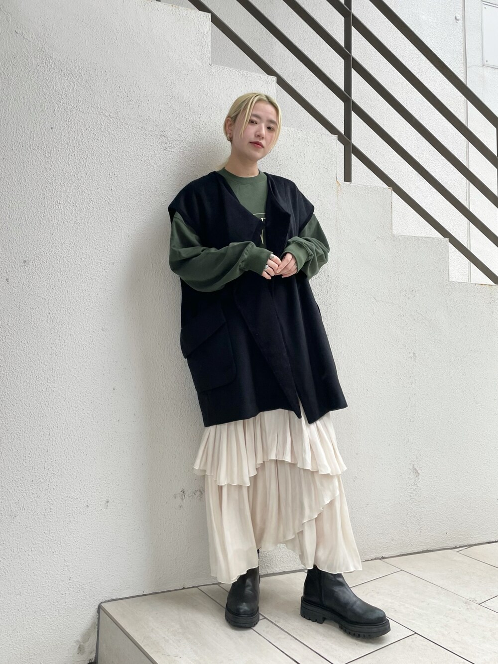 ブラック系のベスト、グリーン系のTシャツ/カットソー、ホワイト系のスカートを着用したレディースの秋コーディネートの1枚目の写真