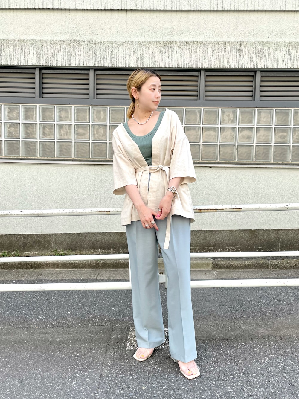 ブルー系のスラックス、ホワイト系のブルゾン、グリーン系のタンクトップを着用したレディースの夏コーディネートの1枚目の写真