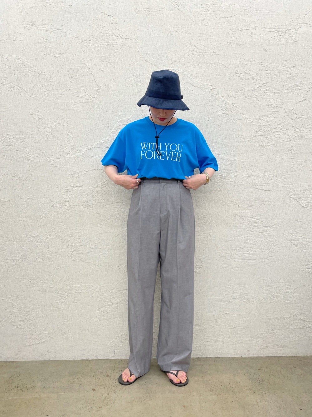 グレー系のスラックス、ブルー系のTシャツ/カットソー、ブルー系のハットを着用したレディースの夏コーディネートの1枚目の写真