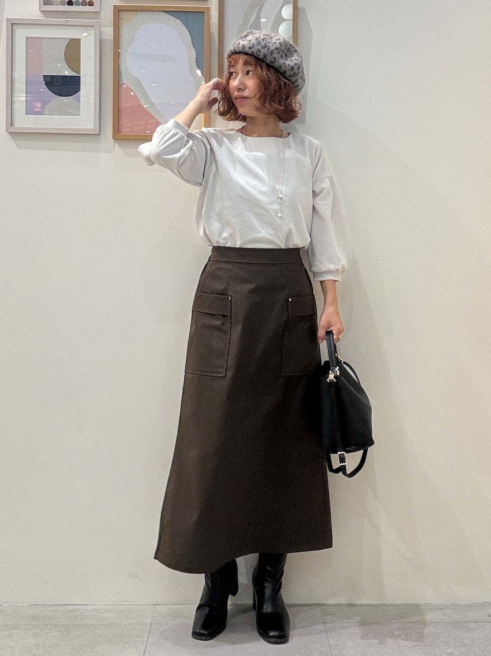 グレー系のTシャツ/カットソー、ブラウン系のスカート、ブラック系のブーツを着用したレディースの秋コーディネートの1枚目の写真