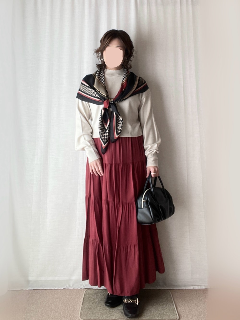 レッド系のスカート、ベージュ系のニット/セーター、グレー系のイヤリングを着用したレディースの秋コーディネートの1枚目の写真