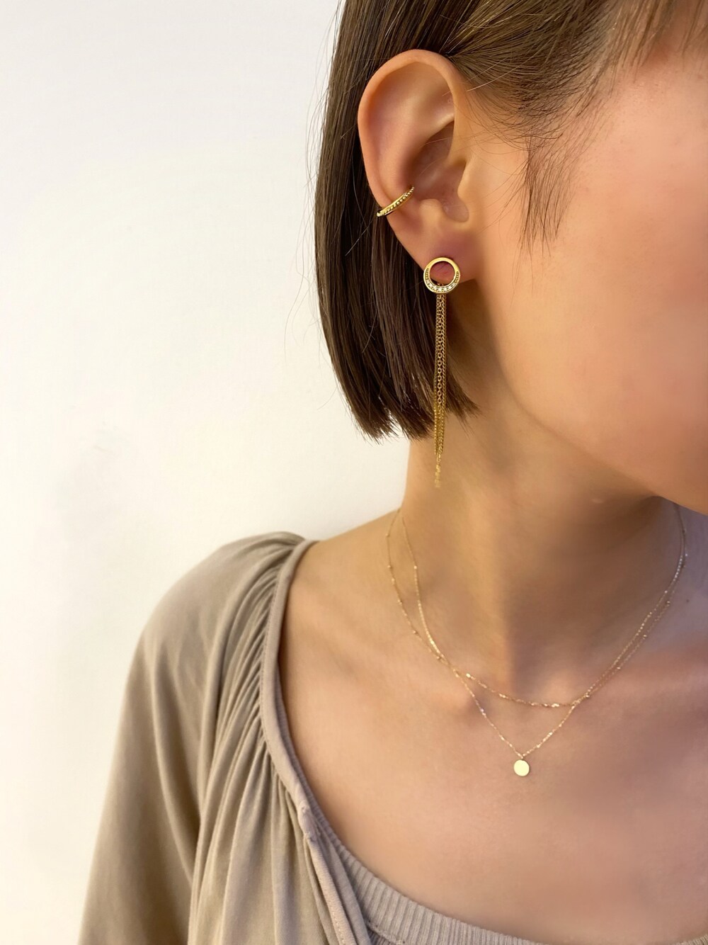 ゴールド系のピアス（片耳用）、ゴールド系のイヤーカフ、ゴールド系のネックレスを着用したレディースの秋コーディネートの1枚目の写真