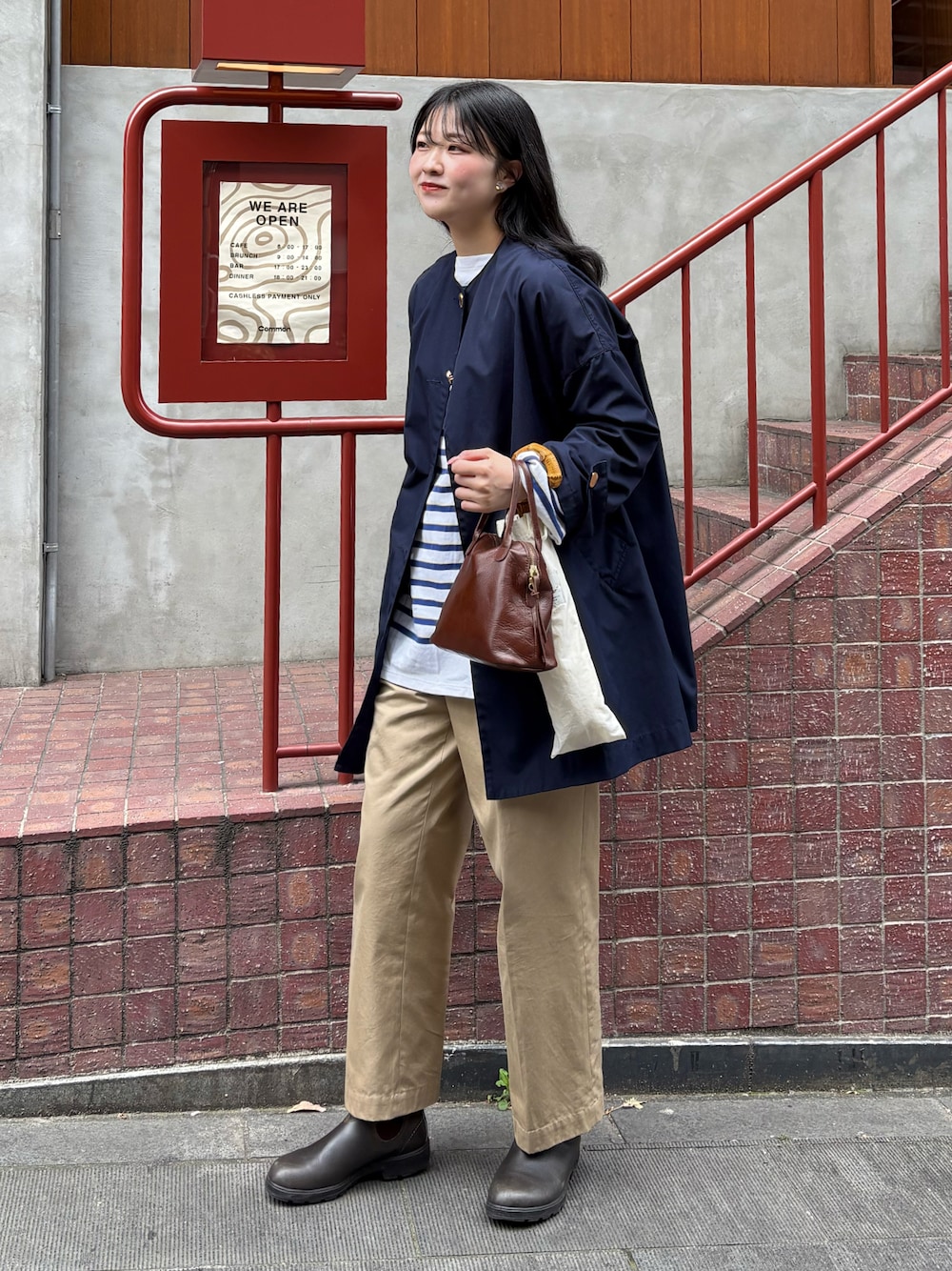 ベージュ系のチノパンツ、ブラウン系のブーツ、ブラウン系のハンドバッグを着用したレディースの春コーディネートの1枚目の写真