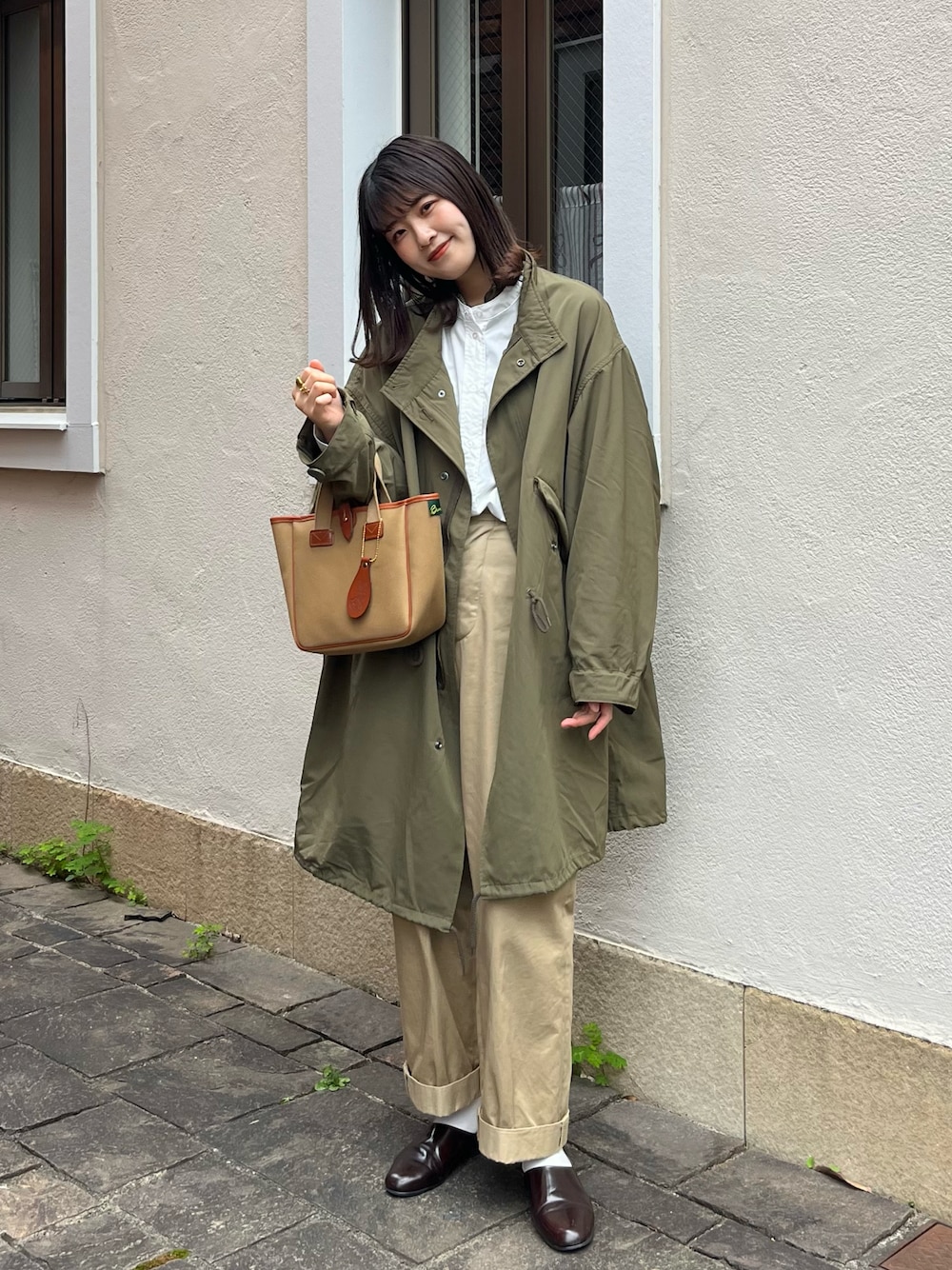 ブラウン系のドレスシューズ、ベージュ系のチノパンツ、グリーン系のトートバッグを着用したレディースの秋コーディネートの1枚目の写真