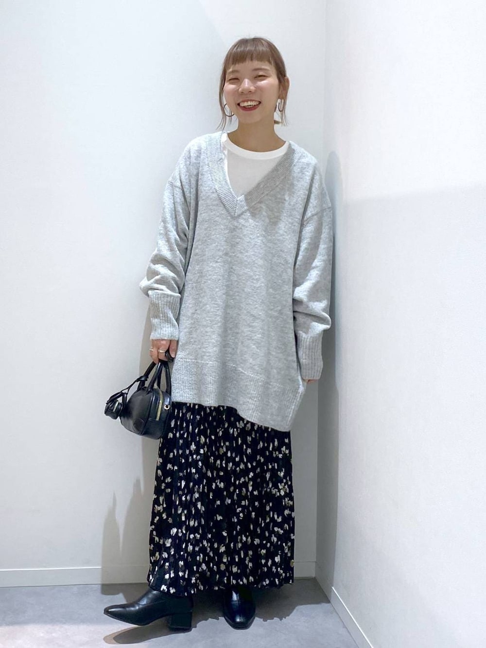 グレー系のニット/セーター、ホワイト系のTシャツ/カットソー、ブラック系のハンドバッグを着用したレディースの秋コーディネートの1枚目の写真