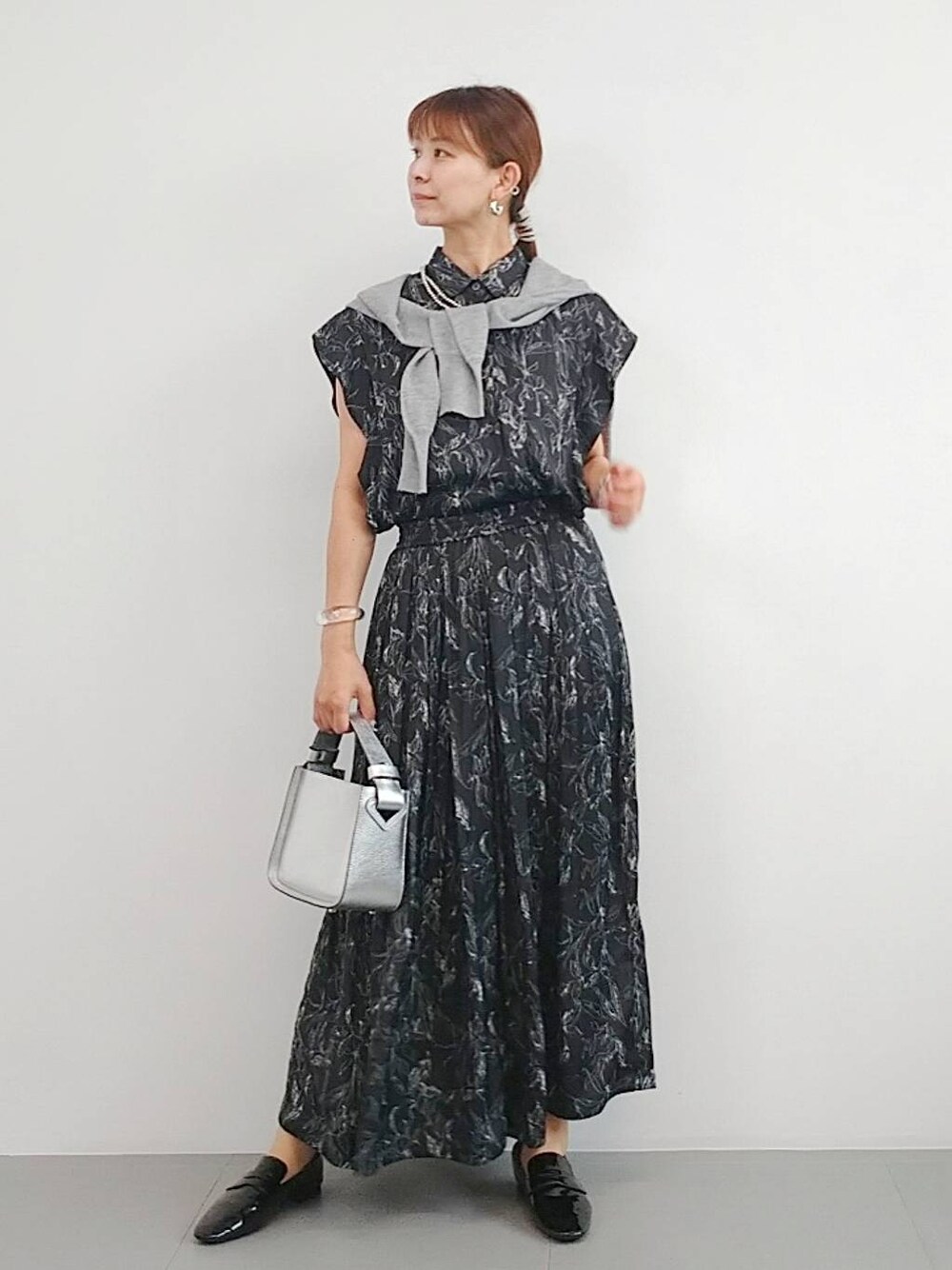 シルバー系のハンドバッグ、ブラック系のレインシューズ、グレー系のカーディガン/ボレロを着用したレディースの夏コーディネートの1枚目の写真