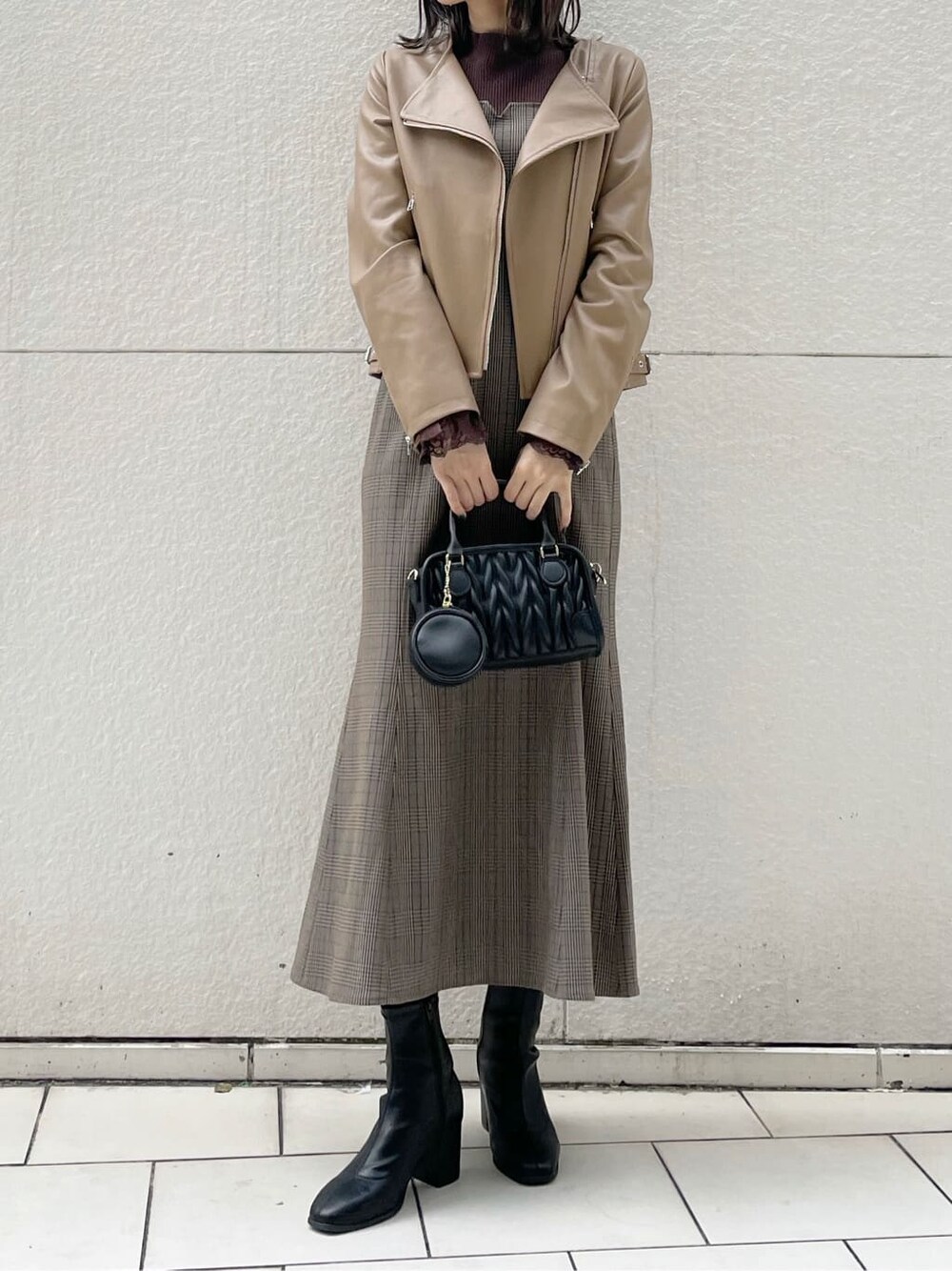 ベージュ系のライダースジャケット、ブラック系のブーツ、その他のジャンパースカートを着用したレディースの秋コーディネートの1枚目の写真
