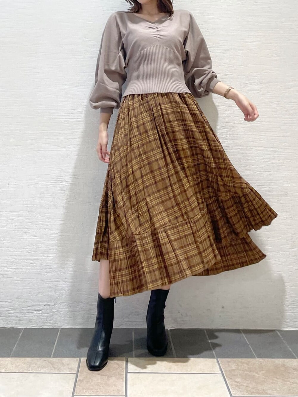 ブラウン系のスカート、ベージュ系のTシャツ/カットソー、ブラック系のブーツを着用したレディースの秋コーディネートの1枚目の写真
