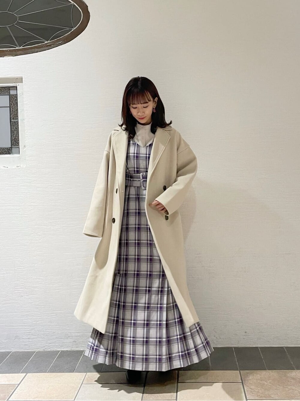 ブラック系のブーツ、ホワイト系のチェスターコート、パープル系のジャンパースカートを着用したレディースの冬コーディネートの1枚目の写真