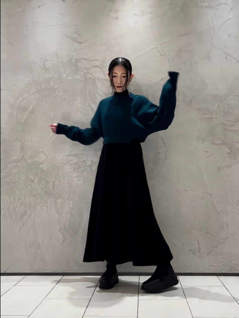 グリーン系のニット/セーター、ブラック系のワンピース、ブラック系のブーツを着用したレディースの秋コーディネートの1枚目の写真