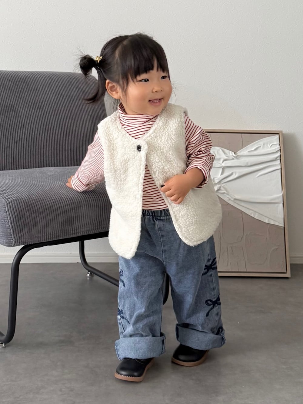 ホワイト系のベスト、レッド系のTシャツ/カットソー、ブルー系のデニムパンツを着用したキッズの秋コーディネートの1枚目の写真