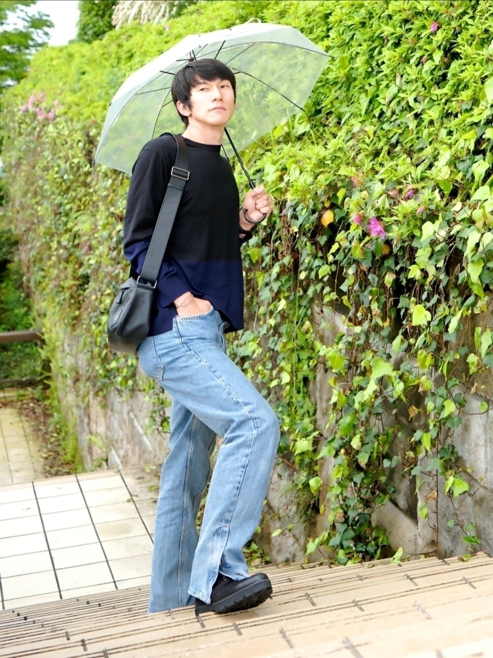 ブラック系のニット/セーター、ブラック系のメッセンジャーバッグ、ブルー系のデニムパンツを着用したメンズの春コーディネートの1枚目の写真