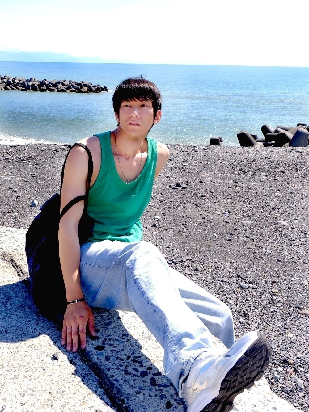 グリーン系のタンクトップ、ブルー系のデニムパンツ、シルバー系のスニーカーを着用したメンズの秋コーディネートの1枚目の写真