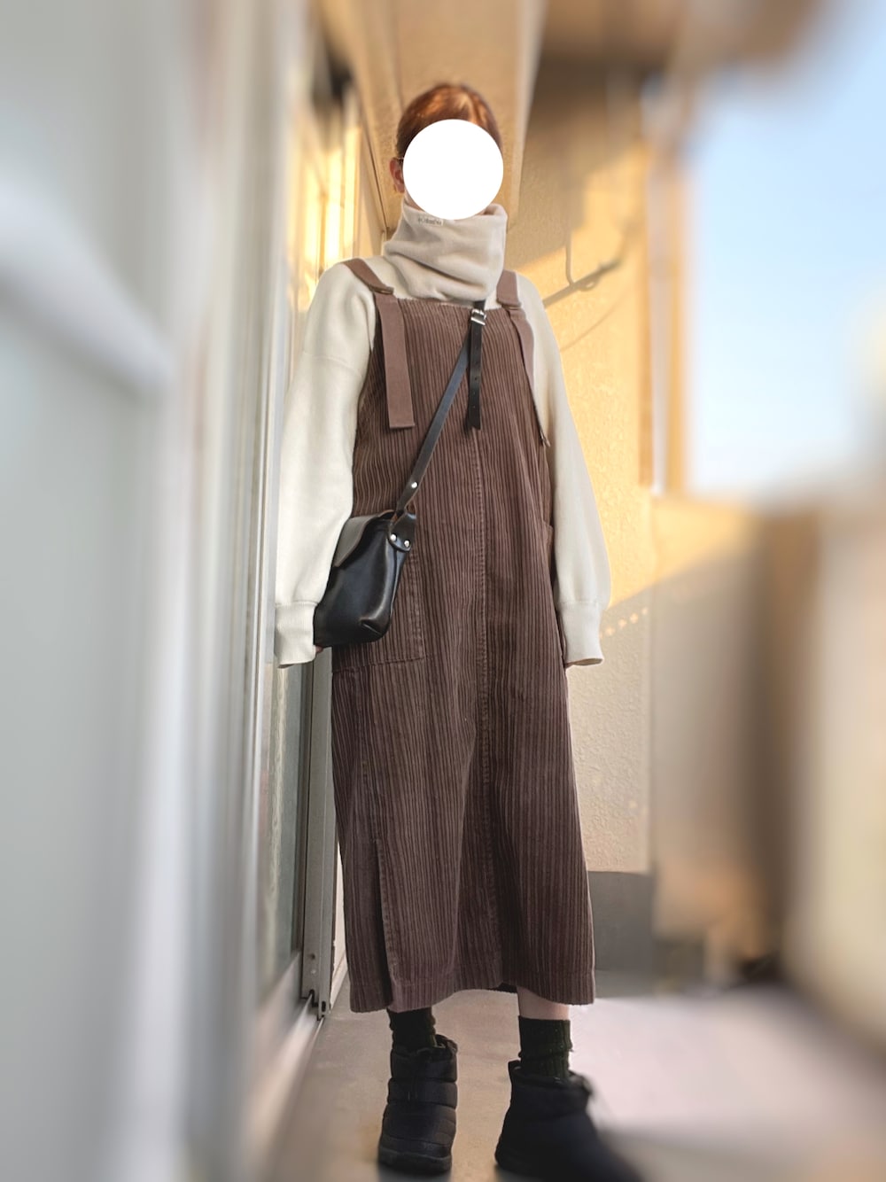 ブラウン系のジャンパースカート、ブラック系のショルダーバッグ、ホワイト系のニット/セーターを着用したレディースの冬コーディネートの1枚目の写真