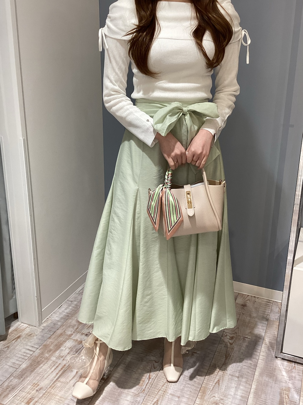 ホワイト系のニット/セーター、ベージュ系のバッグ、グリーン系のスカートを着用したレディースの冬コーディネートの1枚目の写真