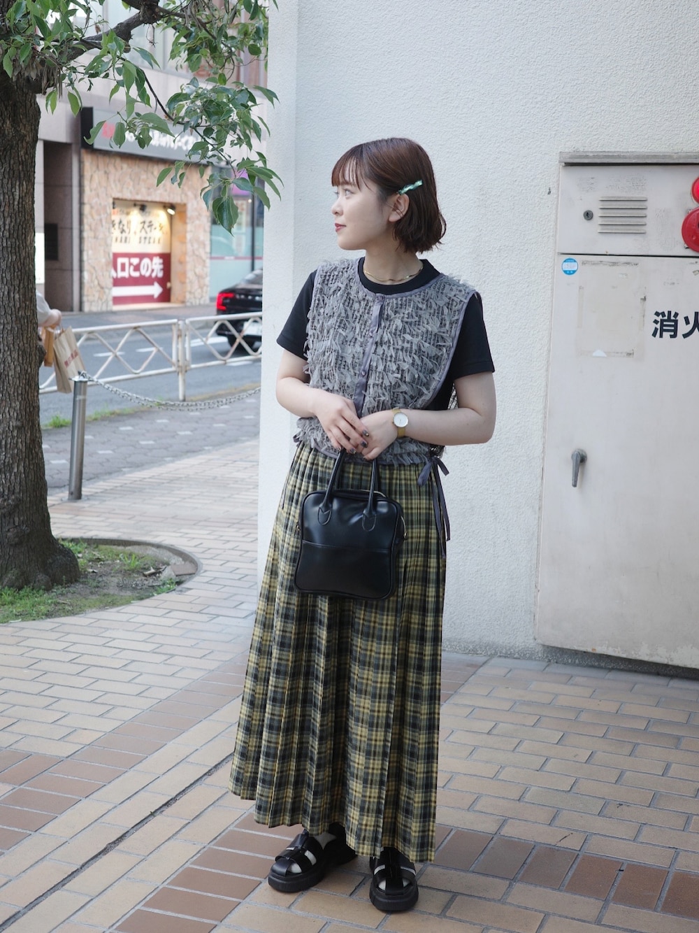 イエロー系のスカート、グレー系のベスト、ブラック系のサンダルを着用したレディースの夏コーディネートの1枚目の写真