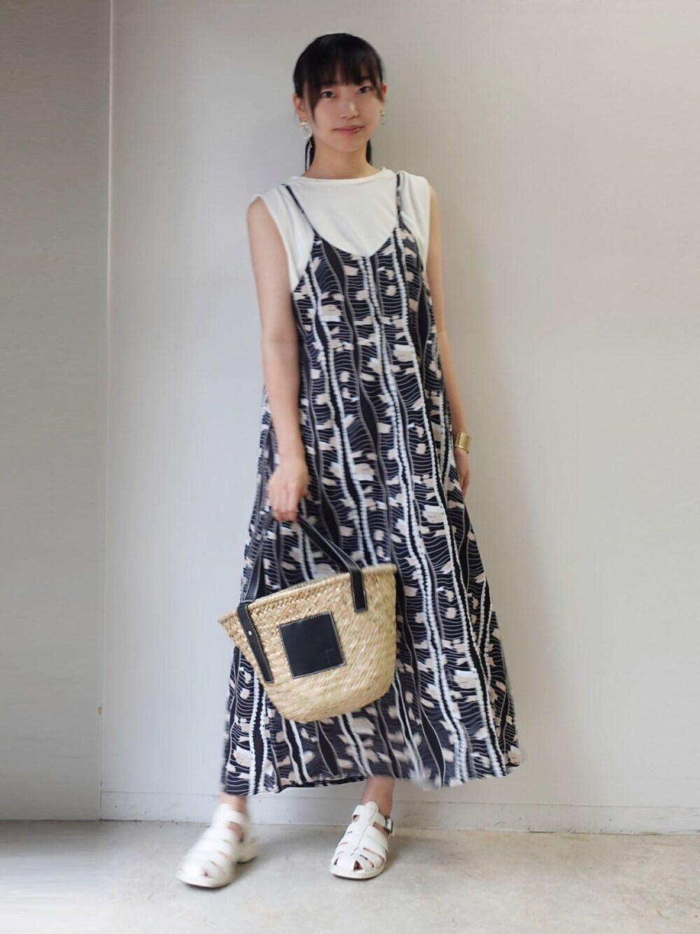 ブラック系のかごバッグ、ブラック系のワンピース、ホワイト系のタンクトップを着用したレディースの夏コーディネートの1枚目の写真