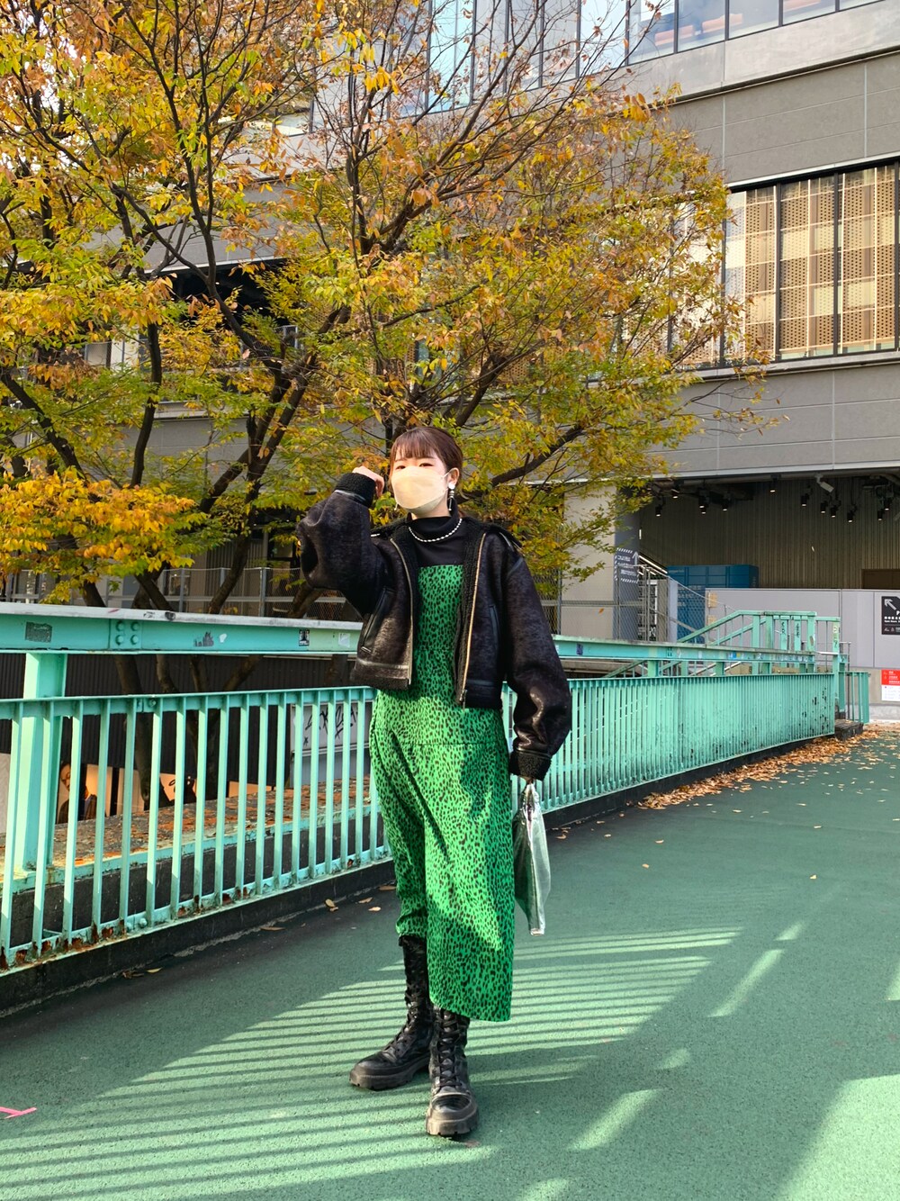 グリーン系のワンピース、ブラック系のブーティ、ブラック系のブルゾンを着用したレディースの秋コーディネートの1枚目の写真