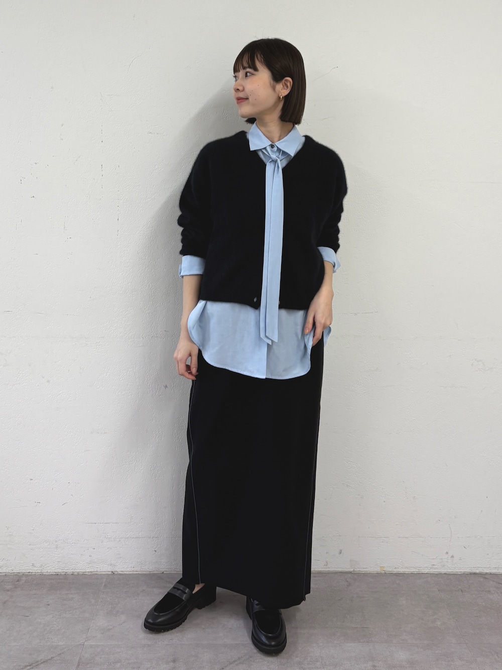 ブラック系のカーディガン/ボレロ、ブルー系のシャツ/ブラウス、ブラック系のスカートを着用したレディースの秋コーディネートの1枚目の写真