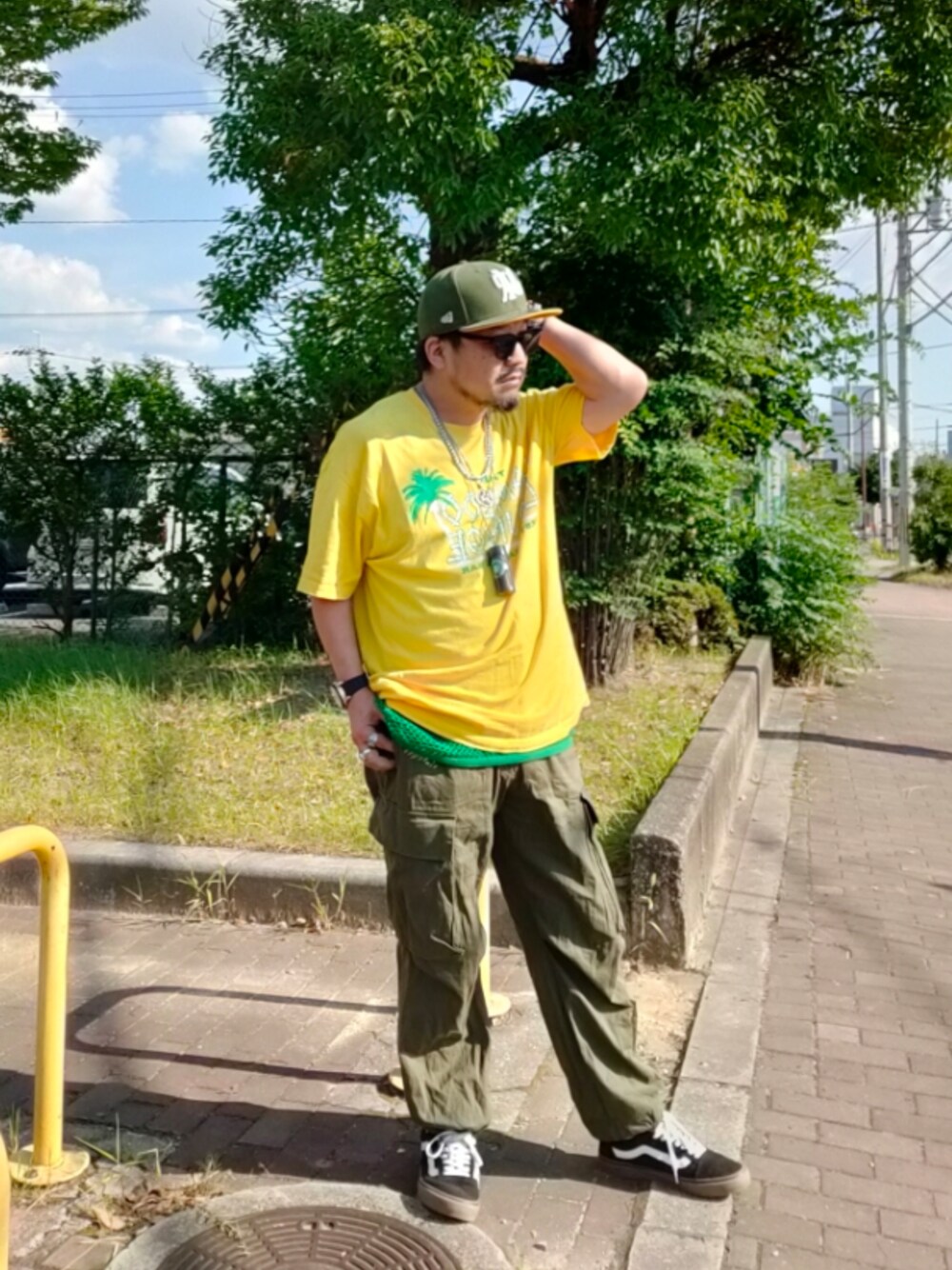 イエロー系のTシャツ/カットソー、グリーン系のタンクトップ、グリーン系のカーゴパンツを着用したメンズの夏コーディネートの1枚目の写真