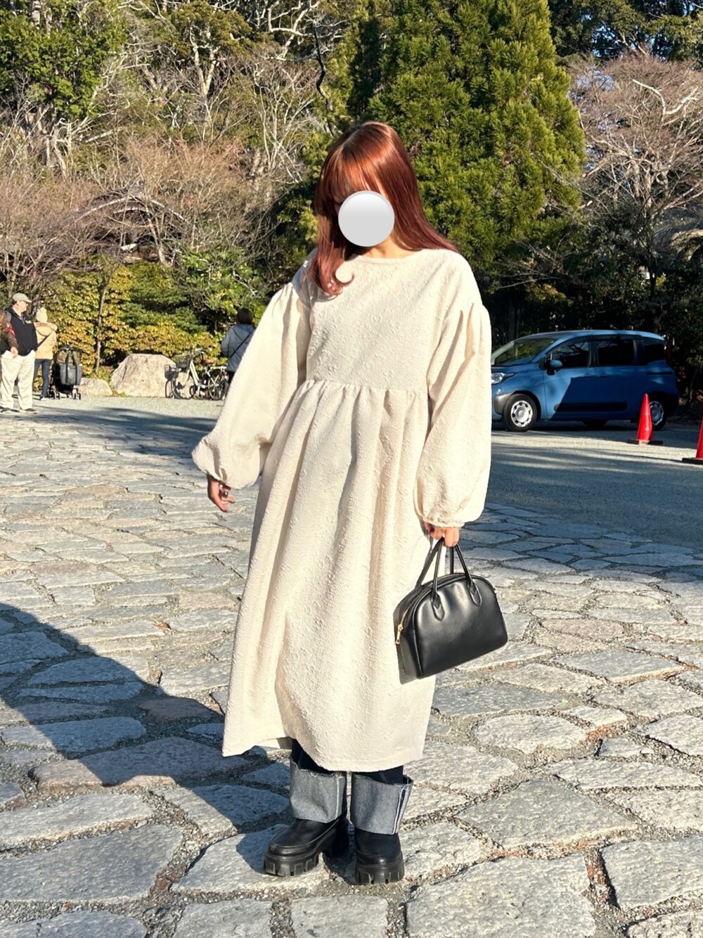 ホワイト系のワンピース、ブルー系のデニムパンツ、ブラック系のブーツを着用したレディースの冬コーディネートの1枚目の写真