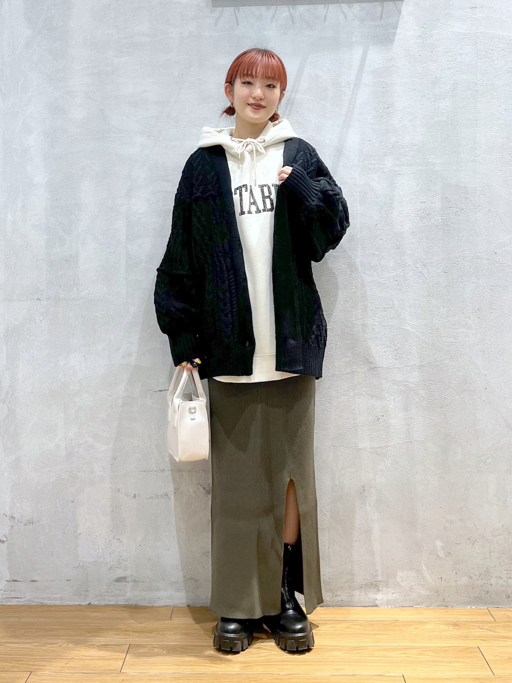 ホワイト系のパーカー、ブラック系のカーディガン/ボレロ、グリーン系のスカートを着用したレディースの秋コーディネートの1枚目の写真