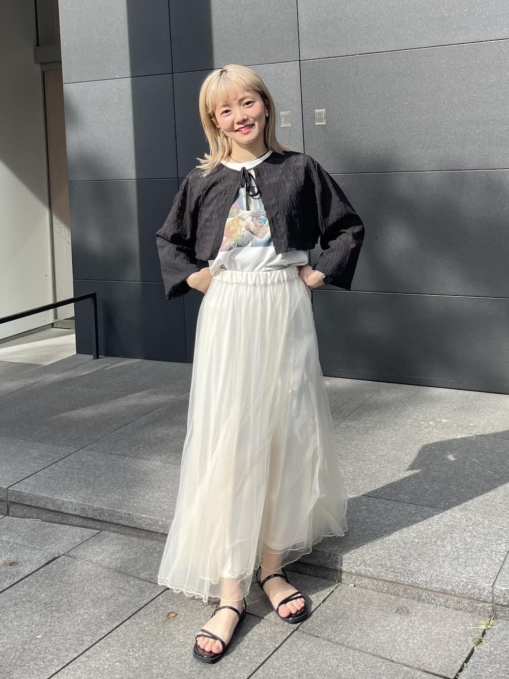 ブラック系のサンダル、ホワイト系のスカート、ブラック系のカーディガン/ボレロを着用したレディースの夏コーディネートの1枚目の写真