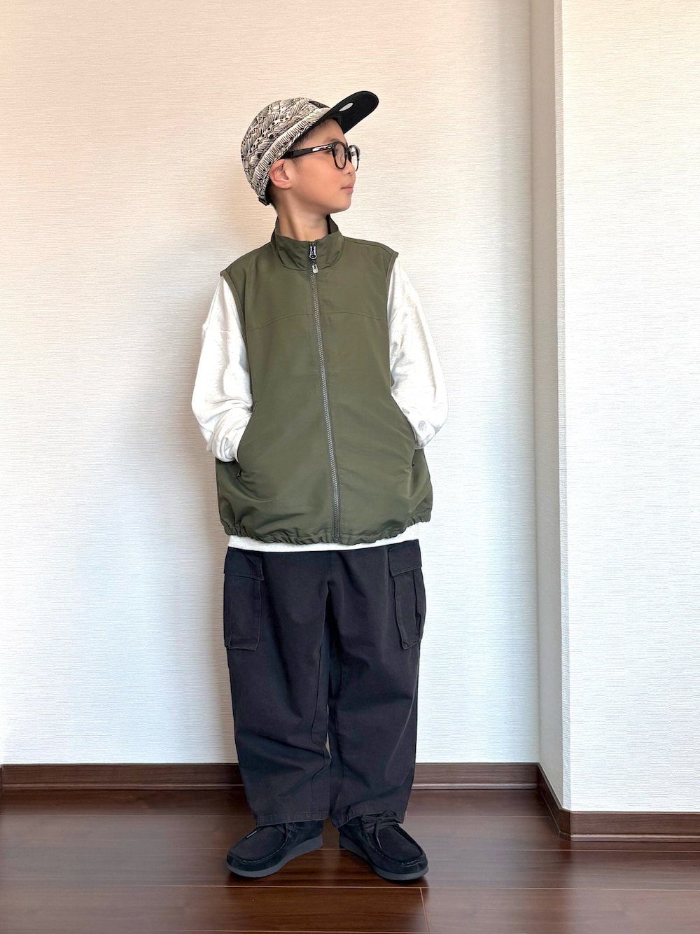 グリーン系のベスト、ブラック系のカーゴパンツ、ベージュ系のスウェットを着用したキッズの冬コーディネートの1枚目の写真