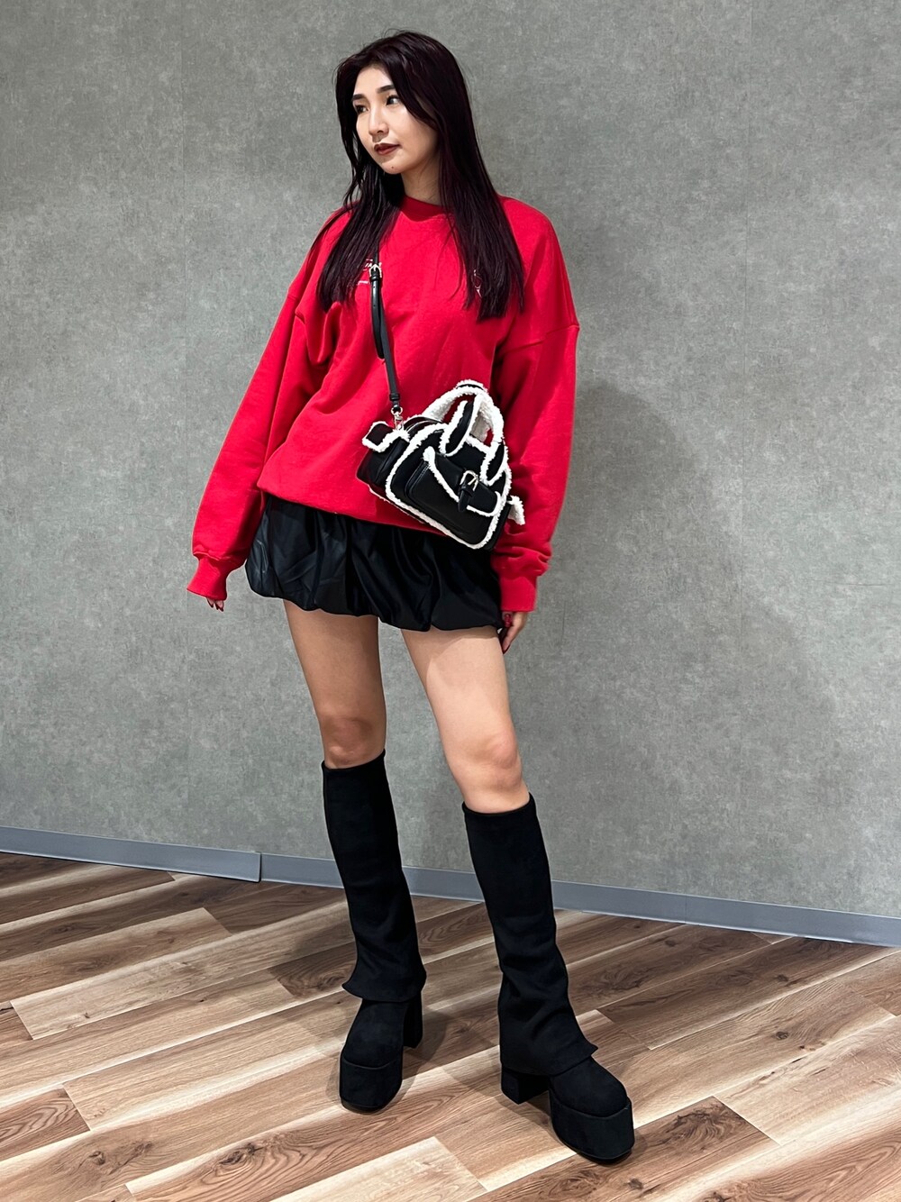 レッド系のスウェット、ブラック系のハンドバッグ、ブラック系のブーツを着用したレディースの秋コーディネートの1枚目の写真