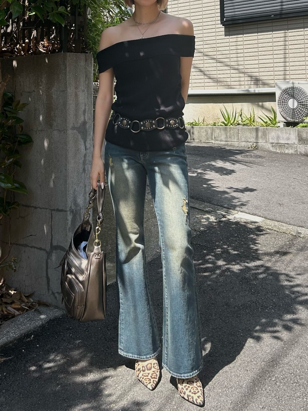 ブルー系のデニムパンツ、ブラック系のニット/セーター、ゴールド系のハンドバッグを着用したレディースの夏コーディネートの1枚目の写真