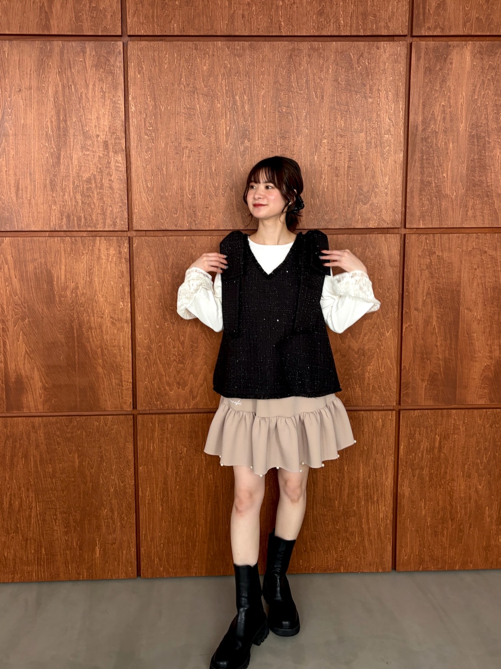 ブラック系のベスト、ベージュ系のスカートを着用したレディースの春コーディネートの1枚目の写真
