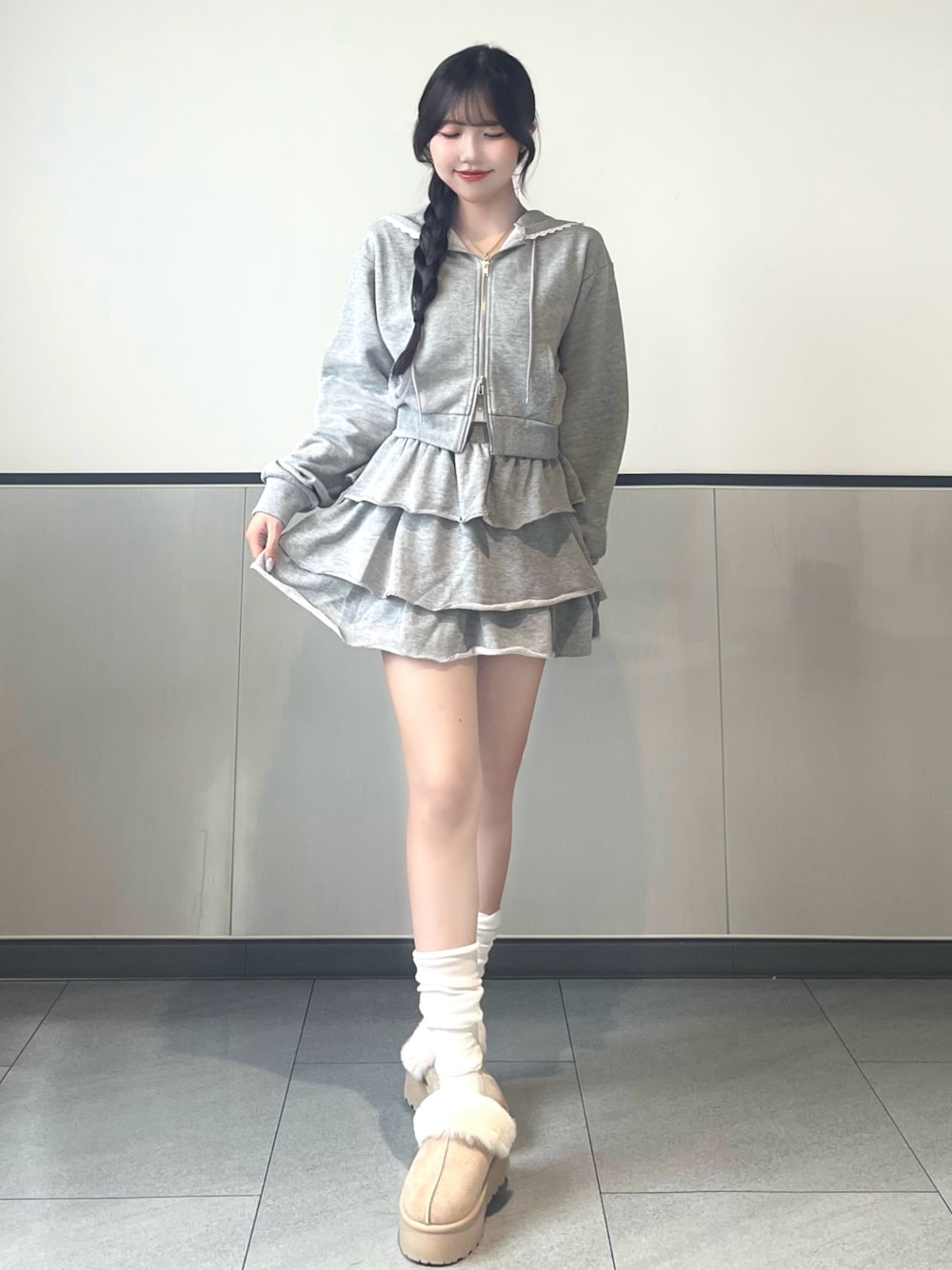 グレー系のパーカー、グレー系のスカート、ベージュ系のブーツを着用したレディースの秋コーディネートの1枚目の写真